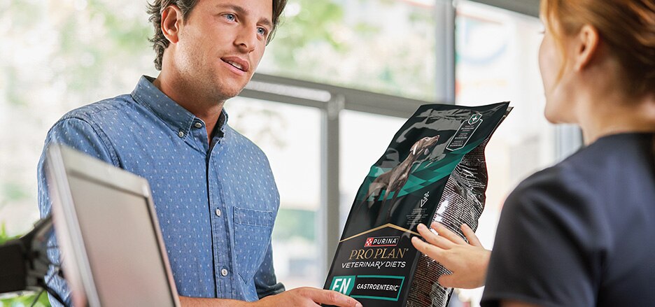 A dog owner purchasing a bag of Pro Plan Veterinary Diets EN Gastroenteric formula at a clinic.